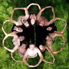 a group of young people standing in a circle on top of green grass, looking up at the camera