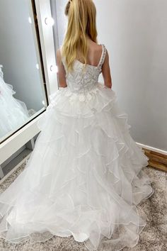 a woman in a white wedding dress looking at herself in the mirror with her back to the camera