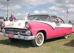 an old pink and white car is parked in the grass