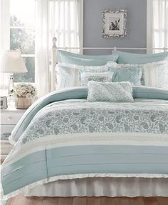 a bed with blue and white comforters in a bedroom next to a window on a wooden floor