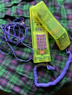 an old cell phone is laying next to a plastic case on a plaid blanket with cords