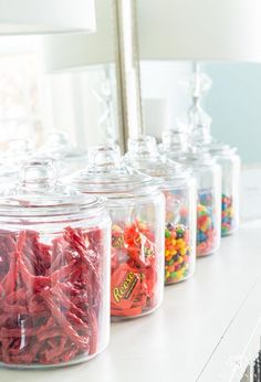 several glass jars filled with candy and candies on top of a white counter next to a mirror