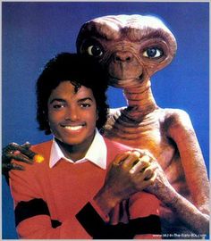 the man is posing with an alien in front of him and another creature behind him