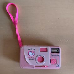 an old pink camera with a hello kitty light on it's strap, sitting on a table