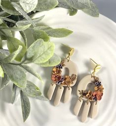 two pairs of earrings with flowers on them sitting on a plate next to a potted plant