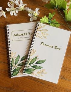 two notebooks sitting on top of a wooden table next to white flowers and leaves