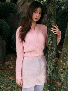 a woman standing next to a tree wearing a pink sweater