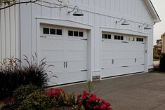 two white garage doors are open in front of a house with red flowers on the driveway