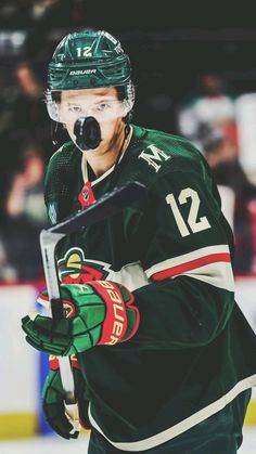 the hockey player is wearing a green uniform and holding a stick in one hand while standing on the ice