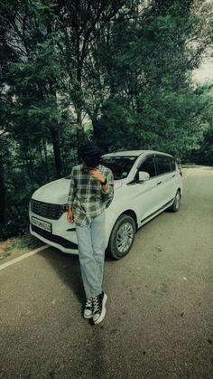 a man standing next to a white car on the side of a road with trees in the background