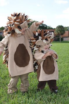 two children dressed up in costumes standing on grass with one holding the other's hand