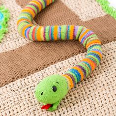 a knitted snake laying on top of a rug next to a stuffed animal toy