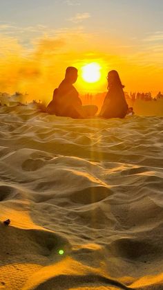 two people sitting in the sand at sunset