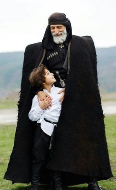 an old man with a child in his lap is posing for the camera while wearing a black cloak