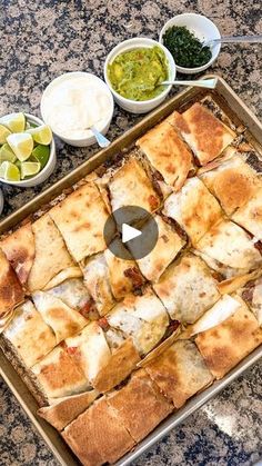 a pan filled with food on top of a counter next to bowls and dips