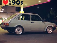 a small gray car parked in front of a gas station at night with the words i love the 90's above it