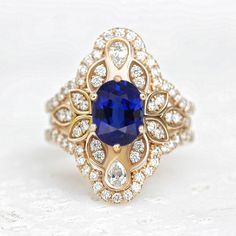 a gold ring with a blue stone surrounded by white and clear diamonds on a white surface