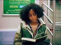 a woman sitting on a train reading a book and listening to headphones with earbuds in her ears