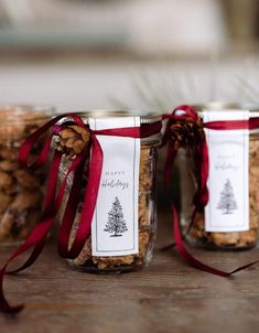 three jars filled with cookies and nuts on top of a wooden table next to a red ribbon