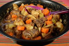 a bowl filled with meat and vegetables on top of a checkered table cloth next to a spoon