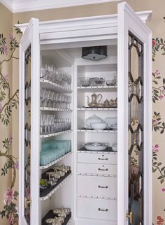 an open cabinet filled with lots of dishes and glasses on top of shelves in a room