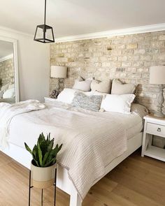 a bedroom with a brick wall and white bed in the corner, potted plant on the floor