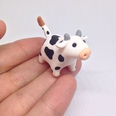 a small toy cow sitting in the palm of someone's hand on a white surface