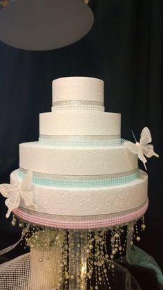 a three tiered wedding cake with white flowers and ribbons on the top, sitting on a table