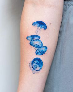 blue ink tattoos on the arm of a woman's left arm, depicting three jellyfish