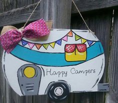 a happy camper sign hanging from a wooden fence with a bow on it's head