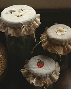 three jars with embroidered designs and strawberries on them