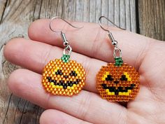 a pair of pumpkin earrings made out of perler beads on a person's hand