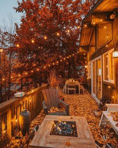 an outdoor deck with lights strung from the ceiling and chairs on it, surrounded by fall leaves