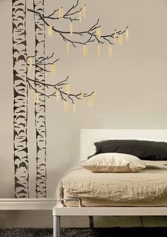 a bed room with a neatly made bed and a tree wall decal