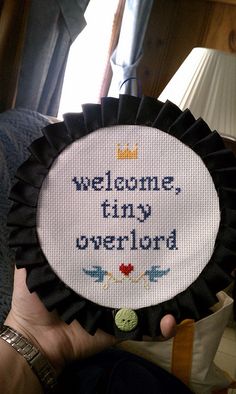 a person holding up a cross - stitch badge with the words welcome tiny over lord