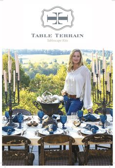 a woman standing in front of a table with blue dishes on it and candles behind her