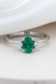 an emerald and diamond ring sitting on top of a white cloth