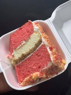 a piece of red cake in a foam container on a black surface with a hand holding it