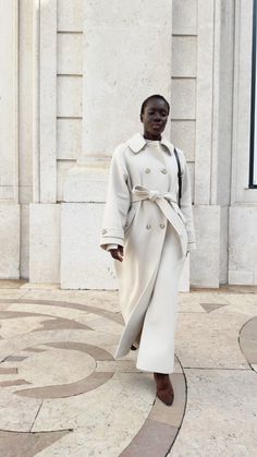 a woman in a white coat is walking down the street