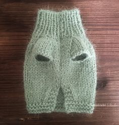 a green knitted mitt with two holes in the middle on a wooden surface