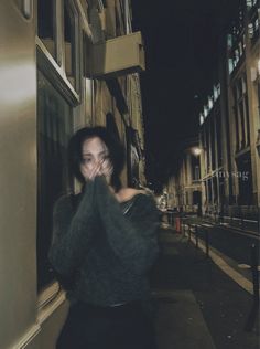 a woman walking down the street at night with her hands on her face and mouth