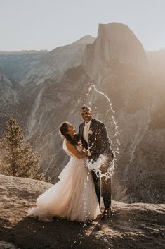 a bride and groom standing on top of a mountain with water splashing from their hands