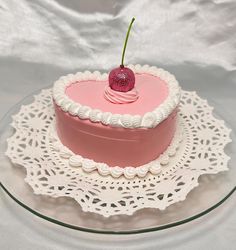 a pink heart shaped cake with a cherry on top sitting on a doily plate