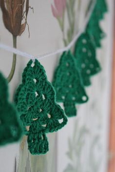 green crocheted christmas tree decorations hanging from a line on a white wall in front of a window