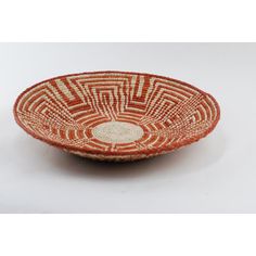 an orange and white woven bowl on a white tablecloth with a circular design in the center