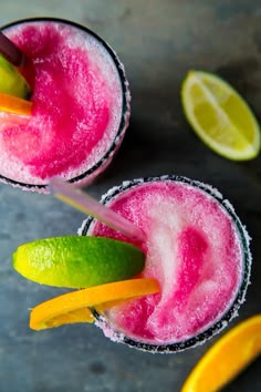 two glasses filled with pink and green drink next to lemon wedges on the rim