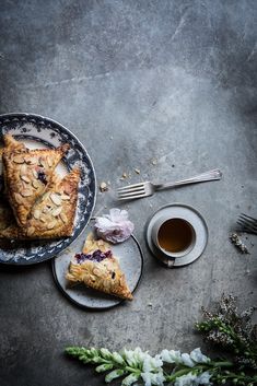 two plates with pies on them next to a cup of tea and silverware