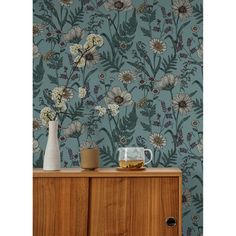 a teal floral wallpaper with white flowers and green leaves on the sideboard