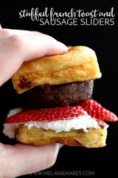 a hand holding a chocolate covered pastry with strawberries and cream on the top, in front of a black background