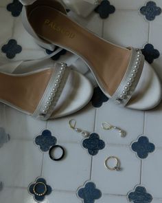 a pair of white shoes sitting on top of a tiled floor next to rings and earrings